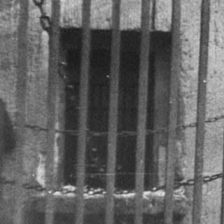 Barred prison cell window with inmate reaching out.