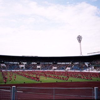 Massive stadium event with synchronized red-clad performers.