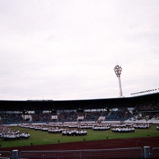 Large stadium ceremony with uniformed groups on field.