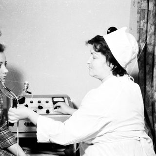 Nurse performing dental examination on patient using early dental equipment.