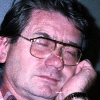 Man sitting indoors, resting chin on hand.