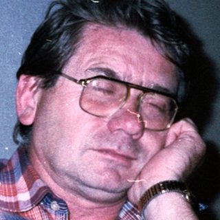 Man sitting indoors, resting chin on hand.
