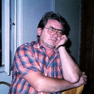 Man sitting indoors, resting chin on hand.