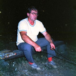 Man sitting alone outdoors at night near water.