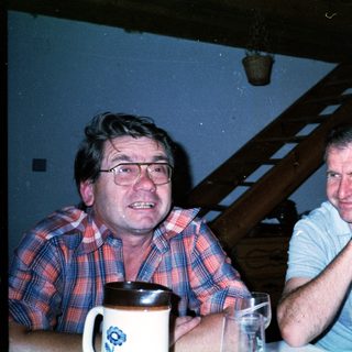 Two men sitting indoors, drinking and conversing.