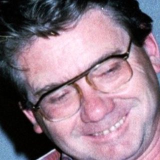 Man smiling indoors wearing plaid shirt.