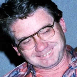 Man smiling indoors wearing plaid shirt.