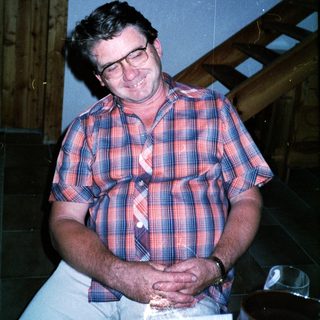 Man smiling indoors wearing plaid shirt.