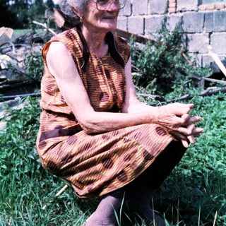 Elderly woman sitting outdoors in patterned dress.