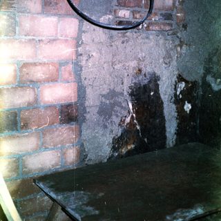 Old wall with exposed bricks, peeling plaster, and rusted metal hook.