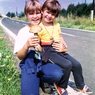 Two children holding mushrooms by the roadside.