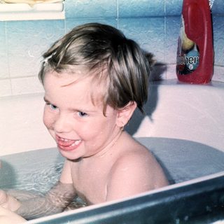 Child happily playing with bath toys in tub.