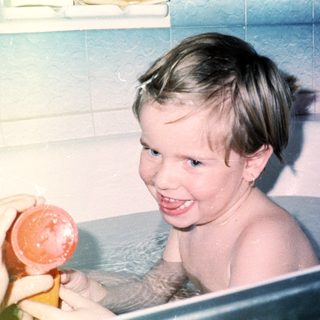 Child happily playing with bath toys in tub.