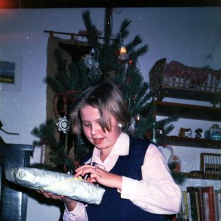 Young girl wrapping holiday gift near decorated Christmas tree.