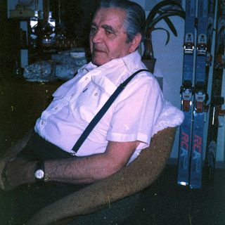Man sitting indoors wearing suspenders and a button-up shirt.