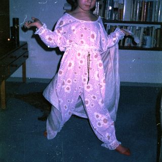 Child in pink polka-dot pajamas dancing indoors.