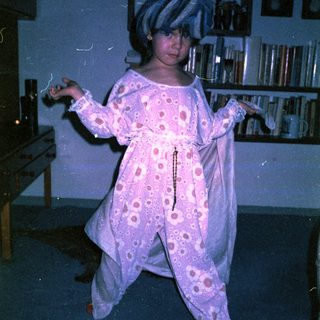 Child in pink polka-dot pajamas dancing indoors.