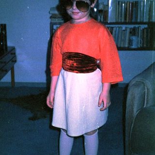 Young child wearing sunglasses, red sweater, and skirt.