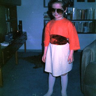 Young child wearing sunglasses, red sweater, and skirt.