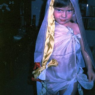 Child dressed in white cloth with head wrapped.
