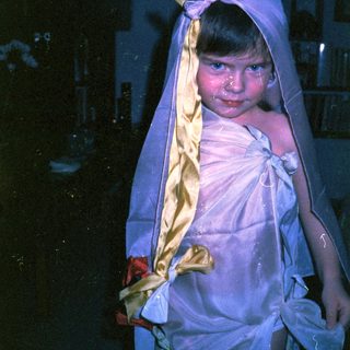 Child dressed in white cloth with head wrapped.