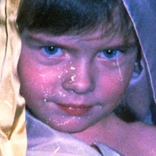Child dressed in white cloth with head wrapped.