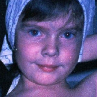 Young girl in polka-dot dress and headscarf indoors.