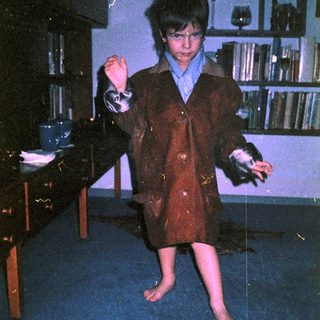Young boy in vintage suit, barefoot, mid-movement indoors.