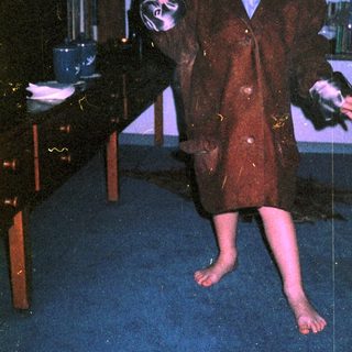 Young boy in vintage suit, barefoot, mid-movement indoors.