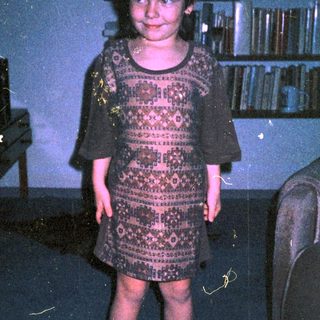 Young girl wearing patterned dress indoors.