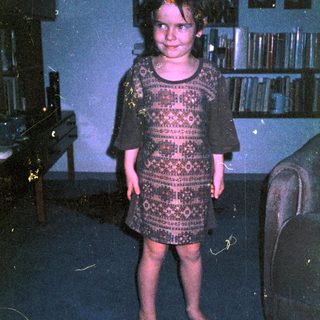 Young girl wearing patterned dress indoors.