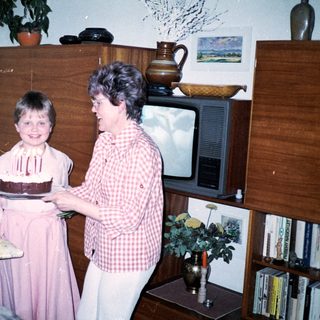 A woman helping a young girl blow out birthday cake candles indoors.