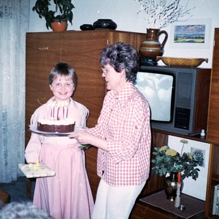 A woman helping a young girl blow out birthday cake candles indoors.