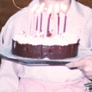 A woman helping a young girl blow out birthday cake candles indoors.