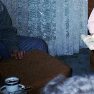 A woman helping a young girl blow out birthday cake candles indoors.