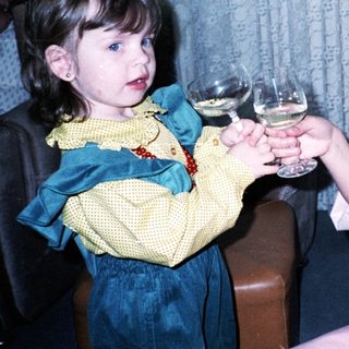 Two children toasting with wine glasses indoors.