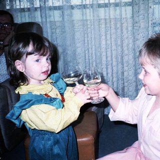 Two children toasting with wine glasses indoors.