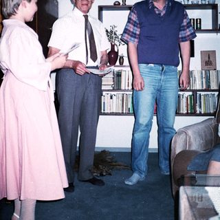 Three people posing indoors with bookshelves in background.