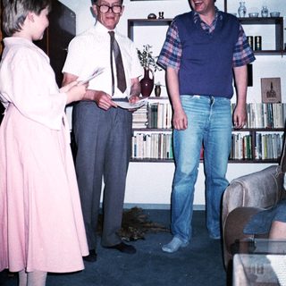 Three people posing indoors with bookshelves in background.