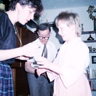 Three people examining a small object indoors.