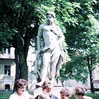 Group of six people posing outdoors near statue.