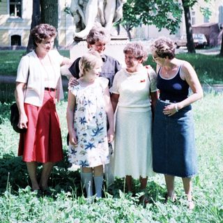Group of six people posing outdoors near statue.