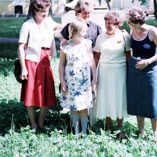 Group of six people posing outdoors near statue.