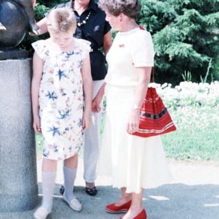 Four women posing with child near Little Mermaid statue.