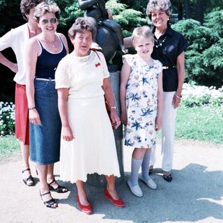 Five women posing together outdoors near statue.