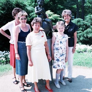 Five women posing together outdoors near statue.