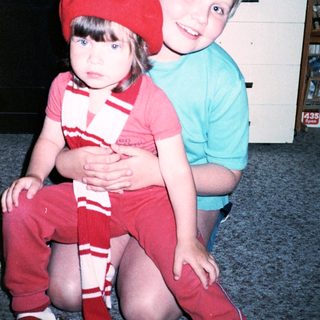 Two children posing indoors, wearing matching red and white outfits.