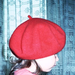 Young girl wearing red beret and shirt playing piano.