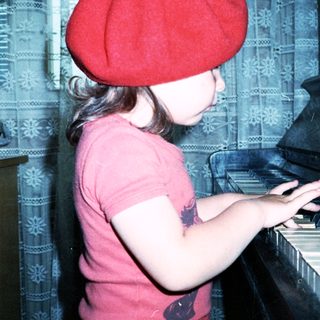Young girl wearing red beret and shirt playing piano.