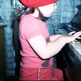 Young girl wearing red beret and shirt playing piano.